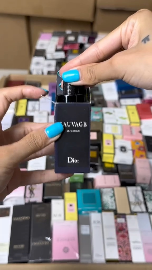 Hands lifting a small perfume bottle from its box with other boxed examples behind it