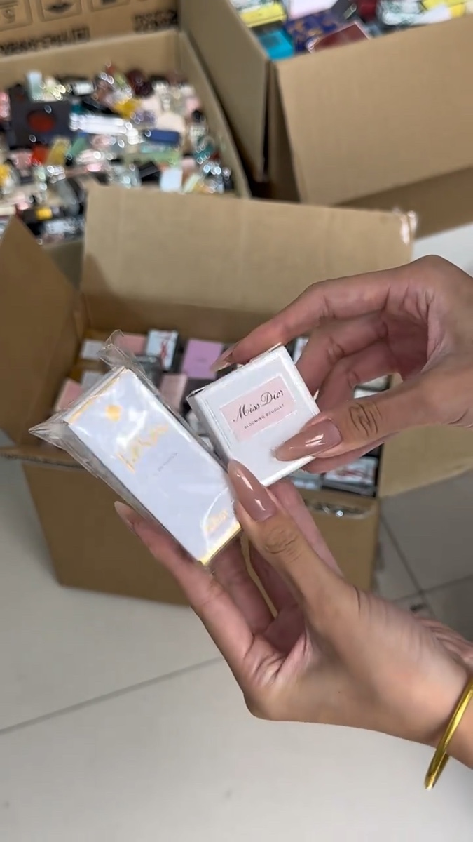 Hands holding small perfume boxes above an open cardboard carton